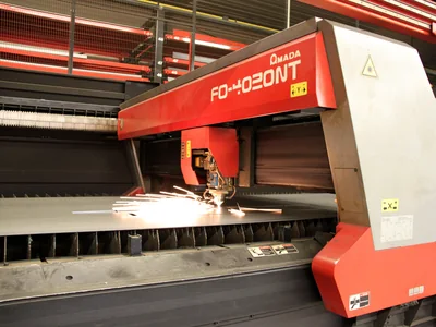 An industrial laser head cuts a sheet of steel and throws sparks across the bed.