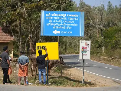 Signage installation crew works on a board beside the road.