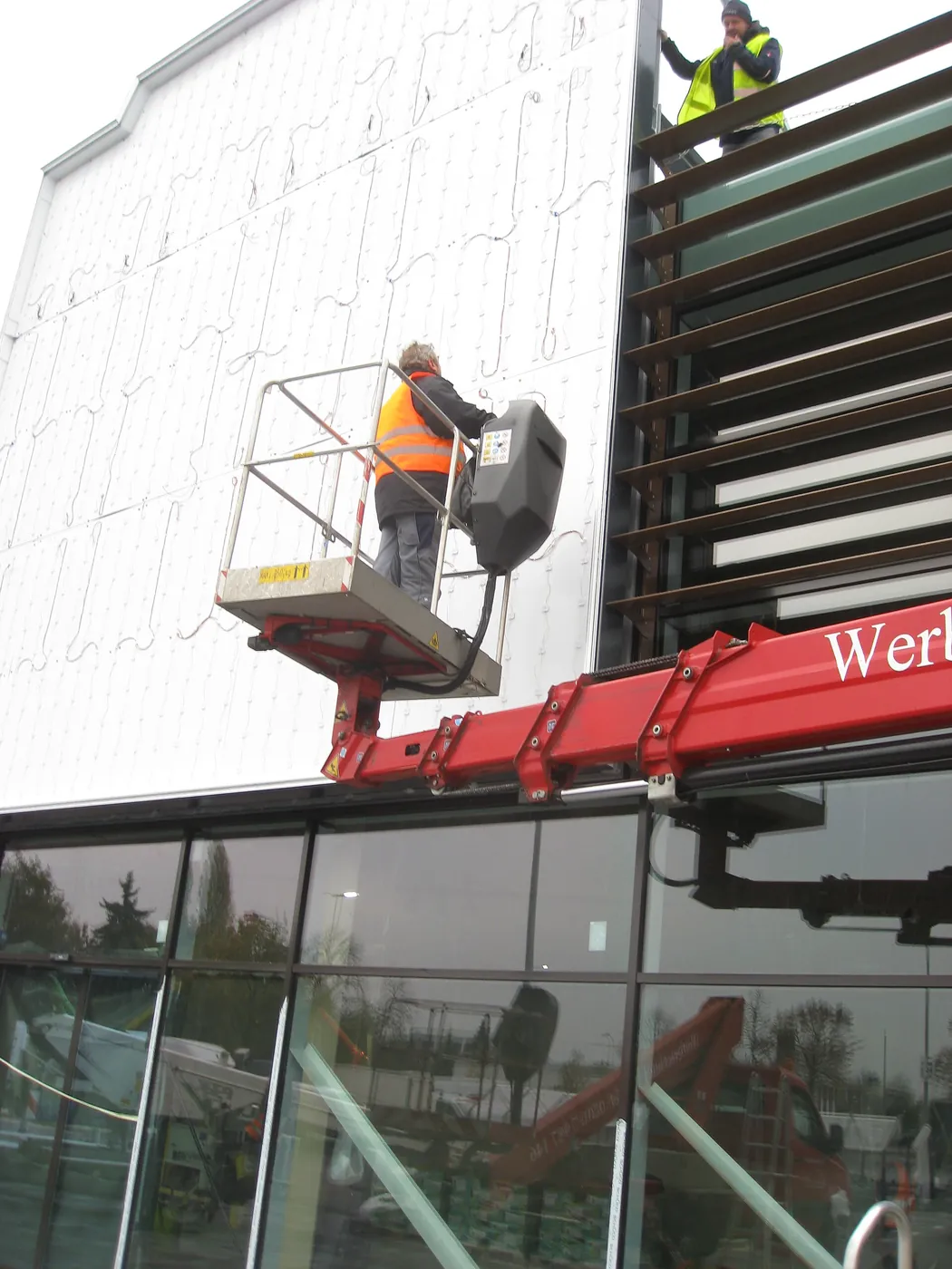Installers on a lift work at a large sign fixed to a building facade.