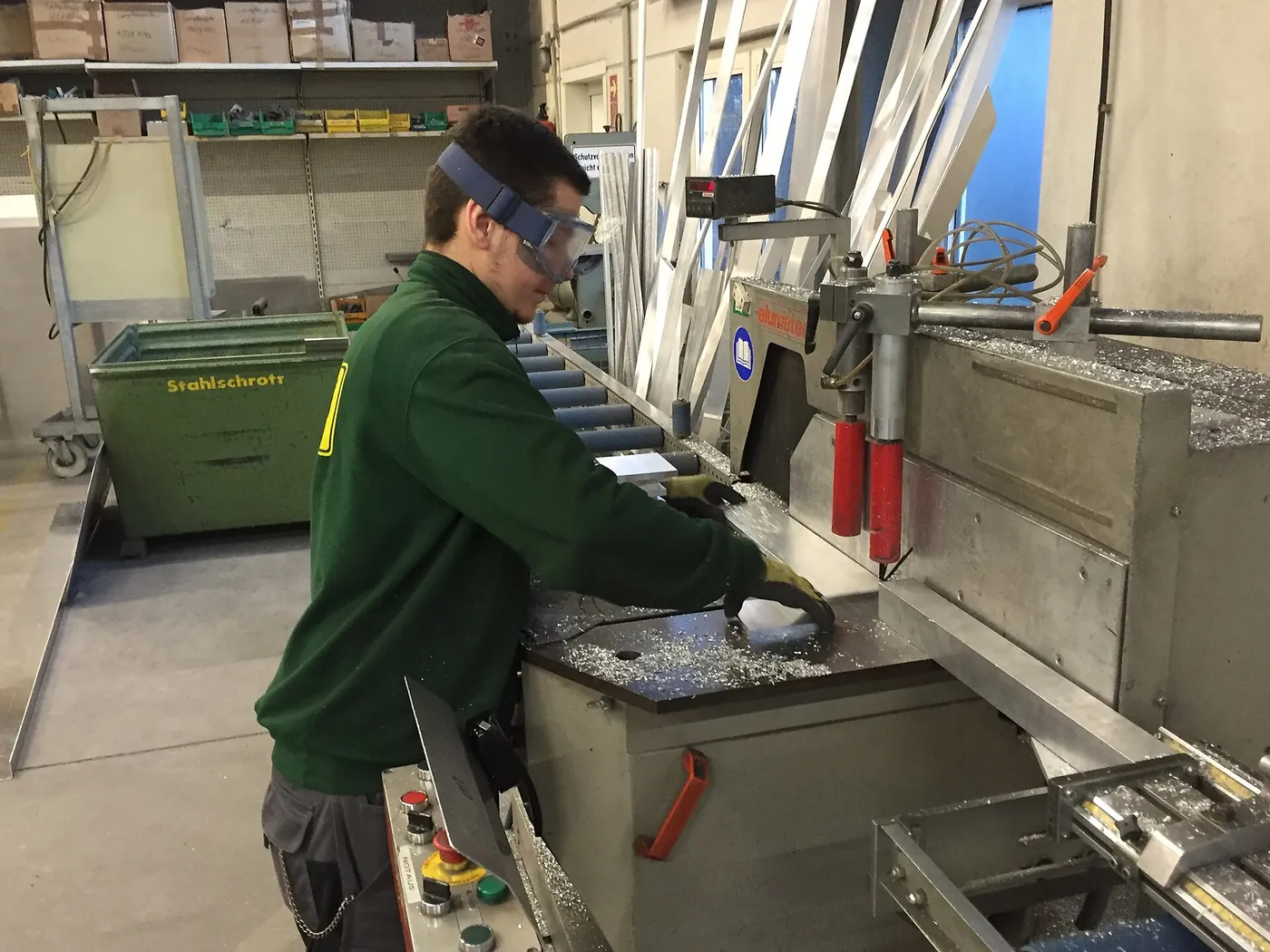 A fabricator cuts an aluminium section to length on a workshop saw.