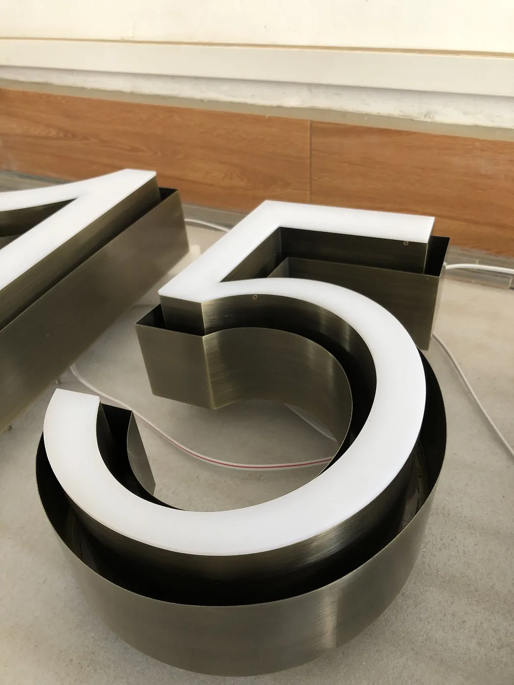 Brushed metal channel letters sit open on the floor with their faces fitted.